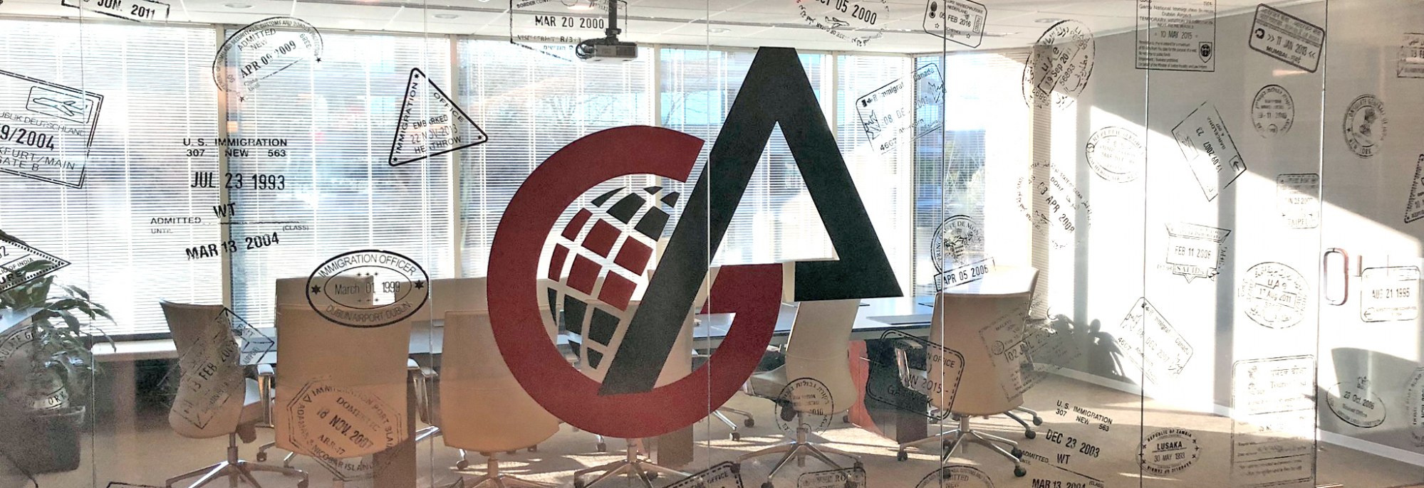 A picture looking through the glass into a large conference room. The glass has visa date stamps and the Goel & Anderson logo styled onto it