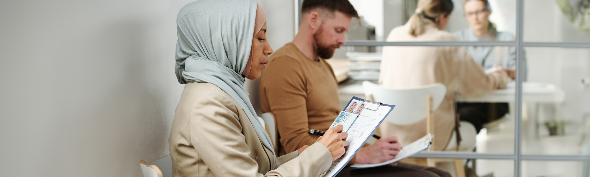 man and muslim woman in hijab sitting on chairs in visa service agency image