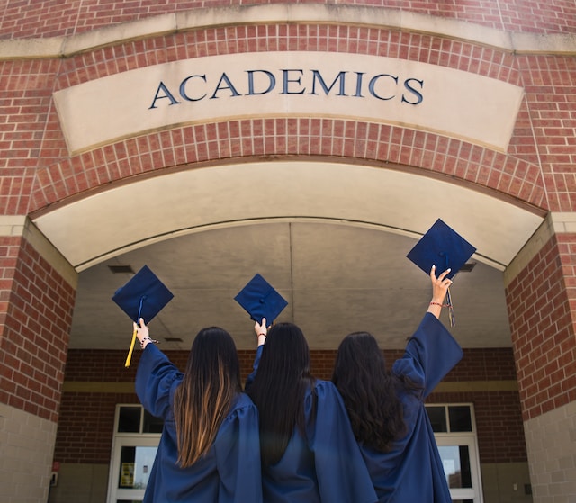 three girls holding graduation caps outside of academic building