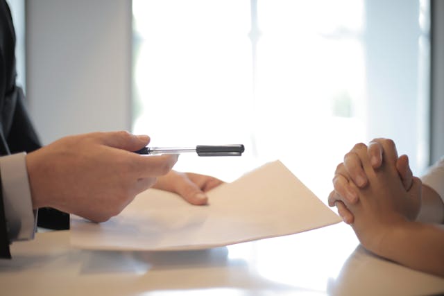 man handing pen and paper to other person image